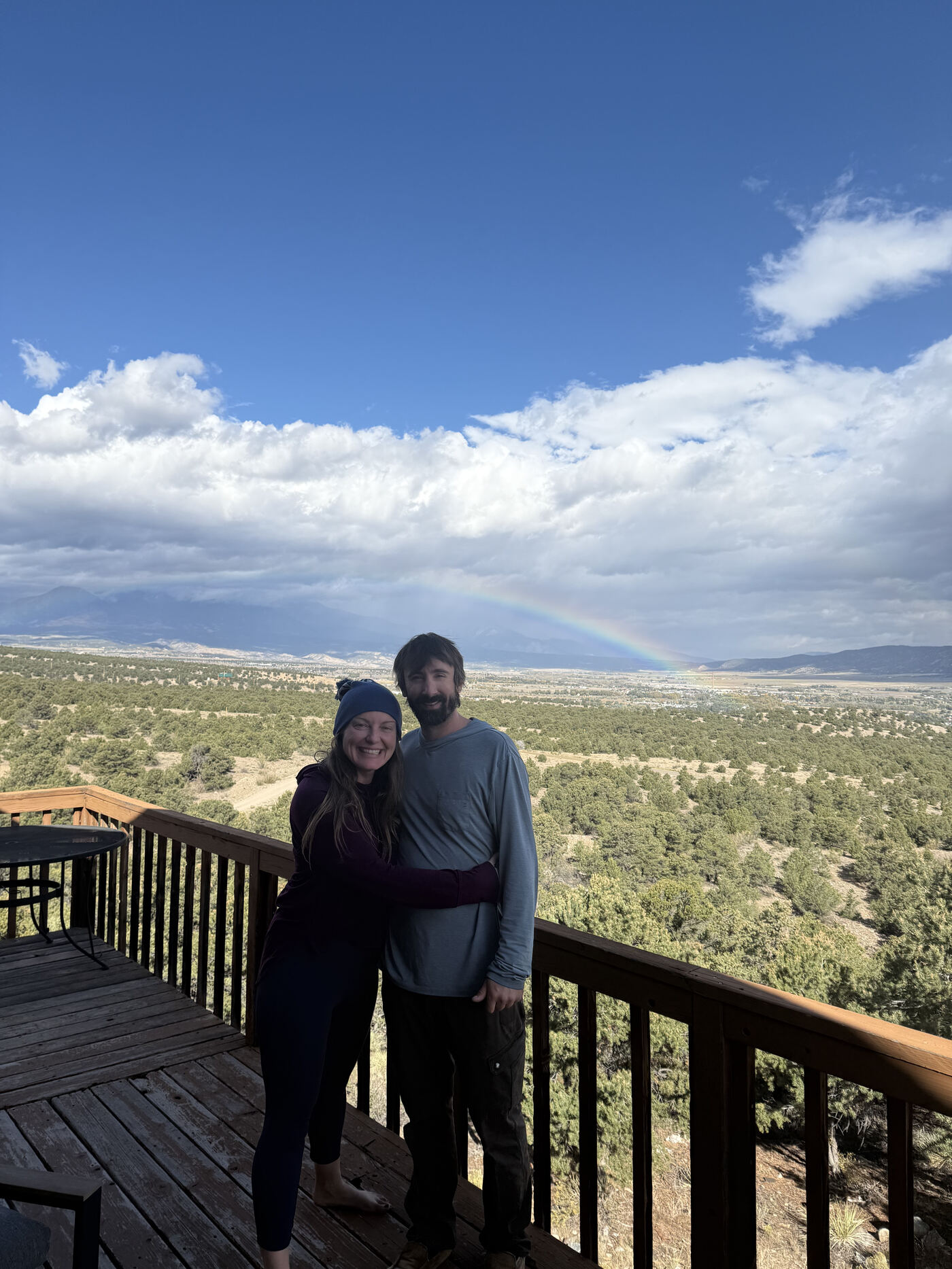 John and Meaghan embracing on the deck of Lot 8 with a faint rainbow over the valley behind them